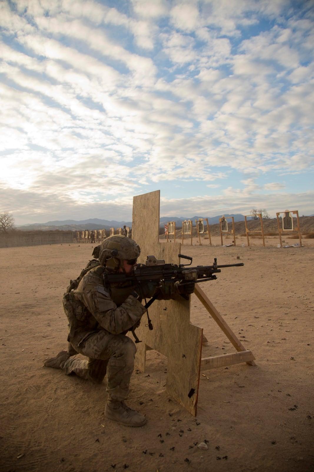 U.S. Army Ranger firing a Mk46 machine gun from a kneeling position beside a barricade on a range