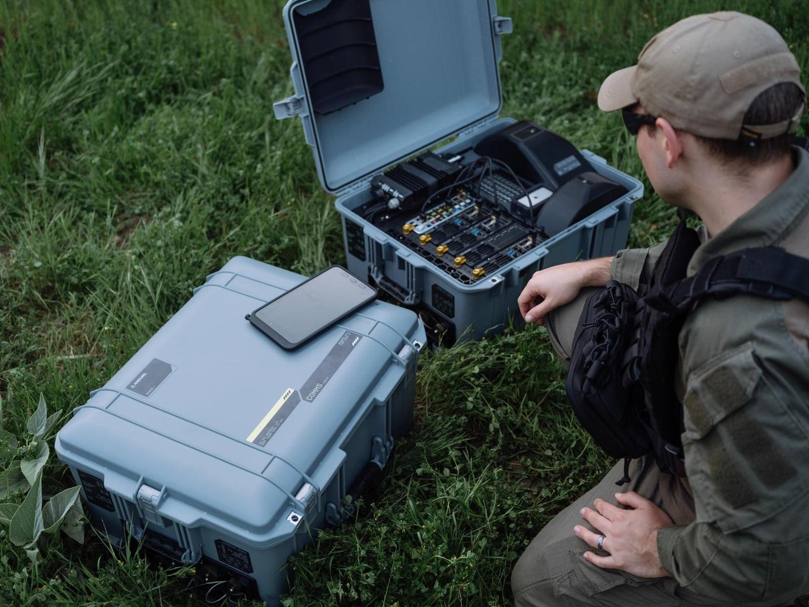 Two open hard-shell cases of rugged electronics on grass beside an operator