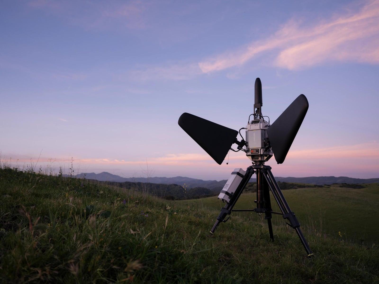 Pulsar on a tripod in a grassy field at dusk with hills behind